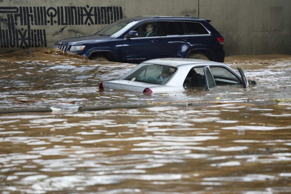 A man, background, drives his car in front a car submerged in flood water at a highway flooded by the rains, in Beirut, Lebanon, Saturday, Dec. 23, 2023. A rainstorm has paralysed parts of Lebanon's cities, turning streets to small rivers, stranding motorists inside their vehicles and damaging homes in some areas. (AP Photo/Hussein Malla)