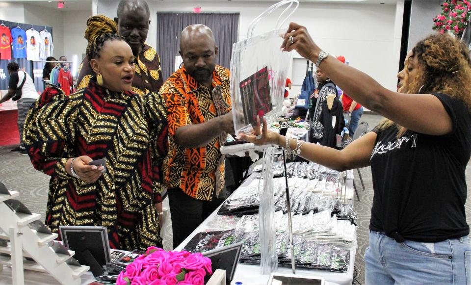 Courtni Williams, right, shows an item to three customers dressed in African-inspired outfits at Saturday's vendor show at the Abilene Convention Center. Williams has created her own business, CookiBloom, to inspire women to be think of themselves as beautiful.