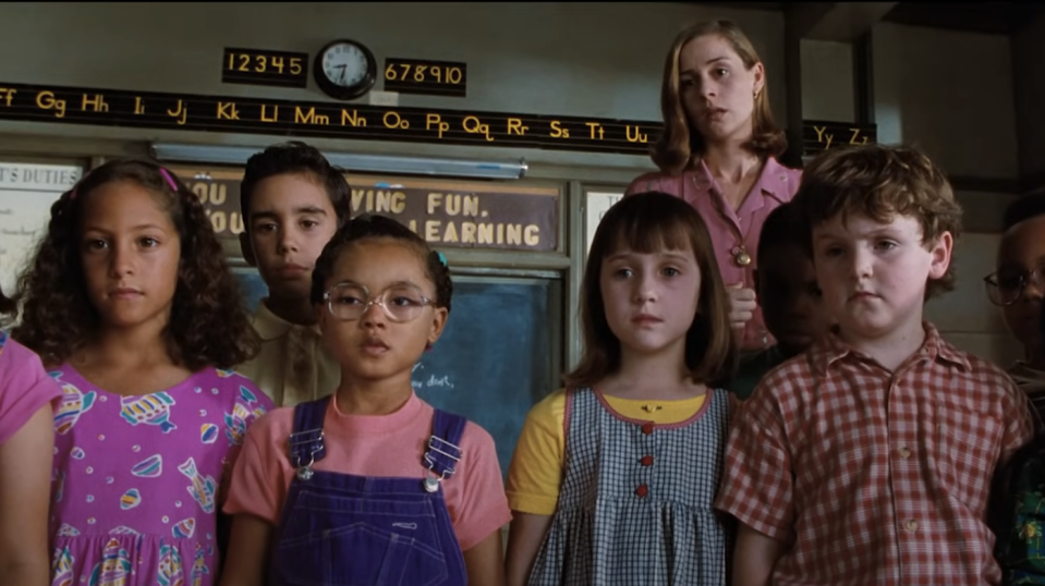 Group of children standing together in a classroom, looking forward