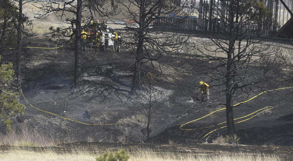 Firefighters work on hot spots in an area that burned trees across from a building under construction, Friday, April 22, 2022, in Colorado Springs, Colo. The fire occurred in a ravine across the road from a heavily populated area along Voyager Parkway, near houses, some still under construction. Homes were evacuated in the area, because of the gusting winds, some up to 50 mph. (Jerilee Bennett/The Gazette via AP)