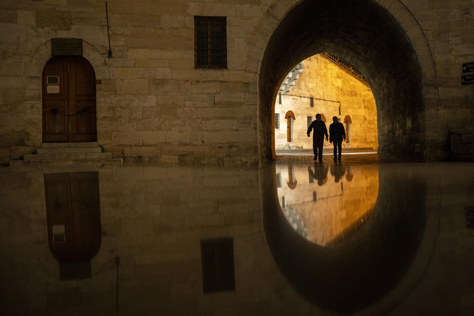 People walk along an alley next to Yeni mosque in Istanbul, Turkey, Monday, March 11, 2024. (AP Photo/Francisco Seco)