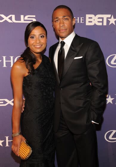 A woman with long black hair wearing a black dress and smiling alongside a man with short black hair wearing a black suit