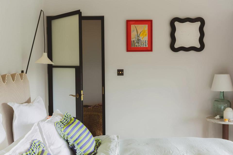 a bedroom with a mirror and a bed and art on the wall, with a black and white door