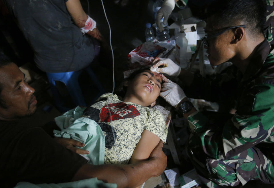 An army doctor examines an injured child outside at Army hospital following earthquakes and a tsunami in Palu, Central Sulawesi, Indonesia, Saturday, Sept. 29, 2018. A tsunami swept away buildings and killed large number of people on the Indonesian island of Sulawesi, dumping victims caught in its relentless path across a devastated landscape that rescuers were struggling to reach Saturday, hindered by damaged roads and broken communications. (AP Photo/Tatan Syuflana)