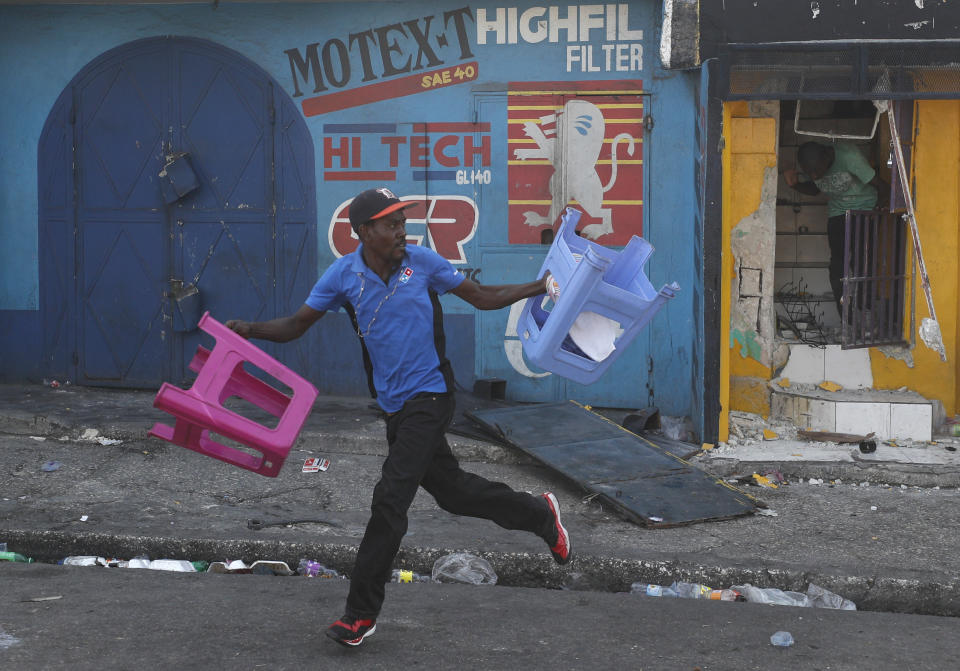 A man loots a couple of plastic stools during an anti-government protest in Port-au-Prince, Haiti, Friday, Oct. 11, 2019. Protesters burned tires and spilled oil on streets in parts of Haiti's capital as they renewed their call for the resignation of President Jovenel Moïse just hours after a journalist was shot to death. (AP Photo/Rebecca Blackwell)