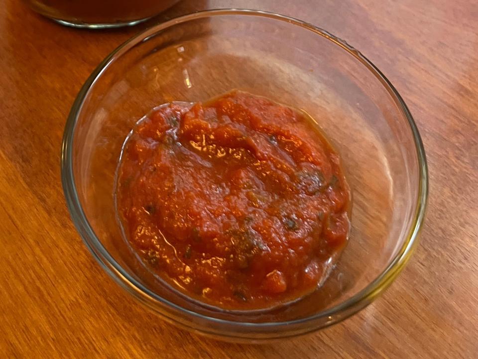 Clear bowl of chunky Primal Kitchen marinara sauce next to jar on a wooden table