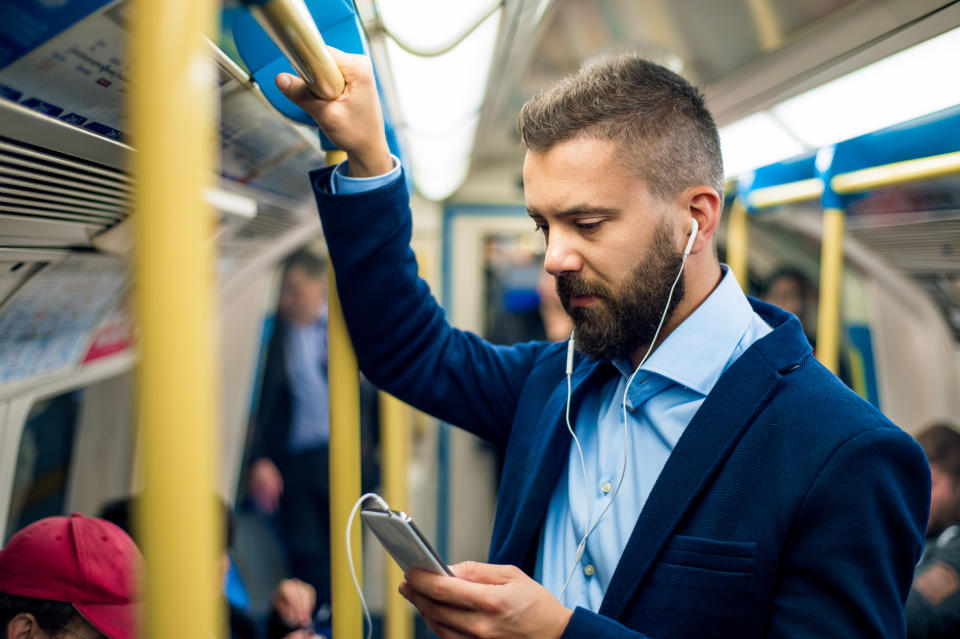 Serious businessman with headphones travelling to work. Standing inside underground wagon, holding handhandle. (Getty Images)