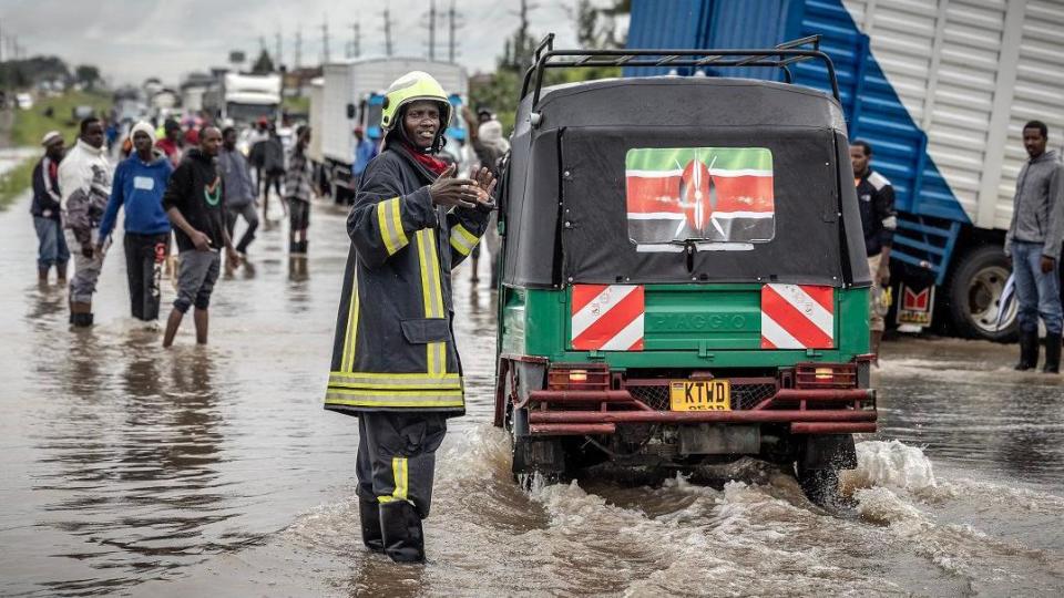 A Kenyan firefighter gives directions people as they travel across a road heavily affected by floods following torrential rains in Kitengela, Kenya.