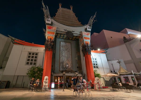 Exterior view of the TCL Chinese Theatre at night with people and a life-sized Oscar statue