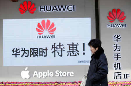 A woman walks past a Huawei and Apple shops in Beijing, China December 12, 2018. REUTERS/Jason Lee