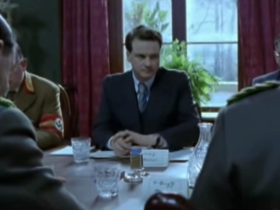 Colin Firth sitting at a table in "Conspiracy."