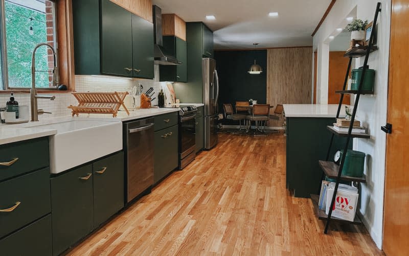 A kitchen with dark green cabinets, a large white sink, and hardwood floors.