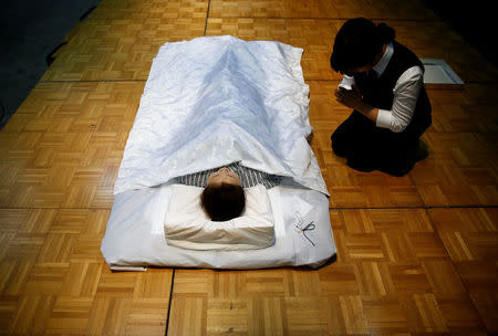 A funeral undertaker prays next to a model during an encoffinment competition at Life Ending Industry EXPO 2017 in Tokyo, Japan August 24, 2017. REUTERS/Kim Kyung-Hoon