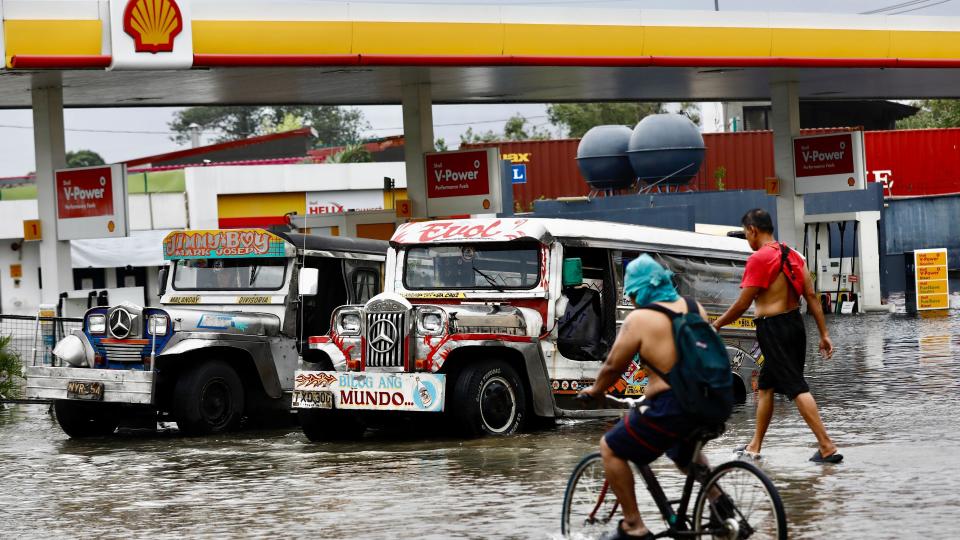 People wade to access a submerged gasoline station in Meycauayan, Bulacan, Philippines