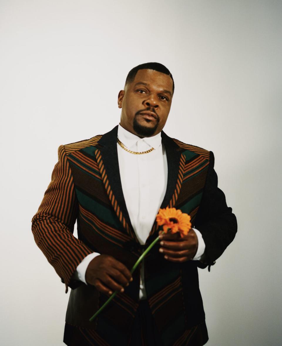 A man in a white shirt and dark jacket stands holding an orange flower