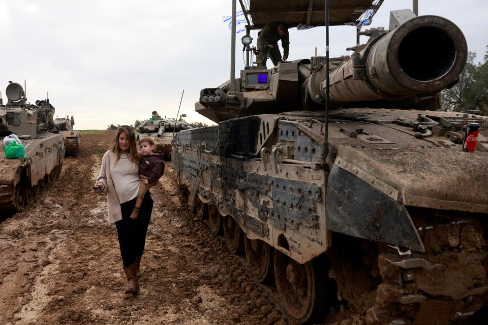 The wife of an Israeli soldier carries her child past a tank, as she visits her husband upon his return from a mission in the Palestinian territory on January 28, 2024.