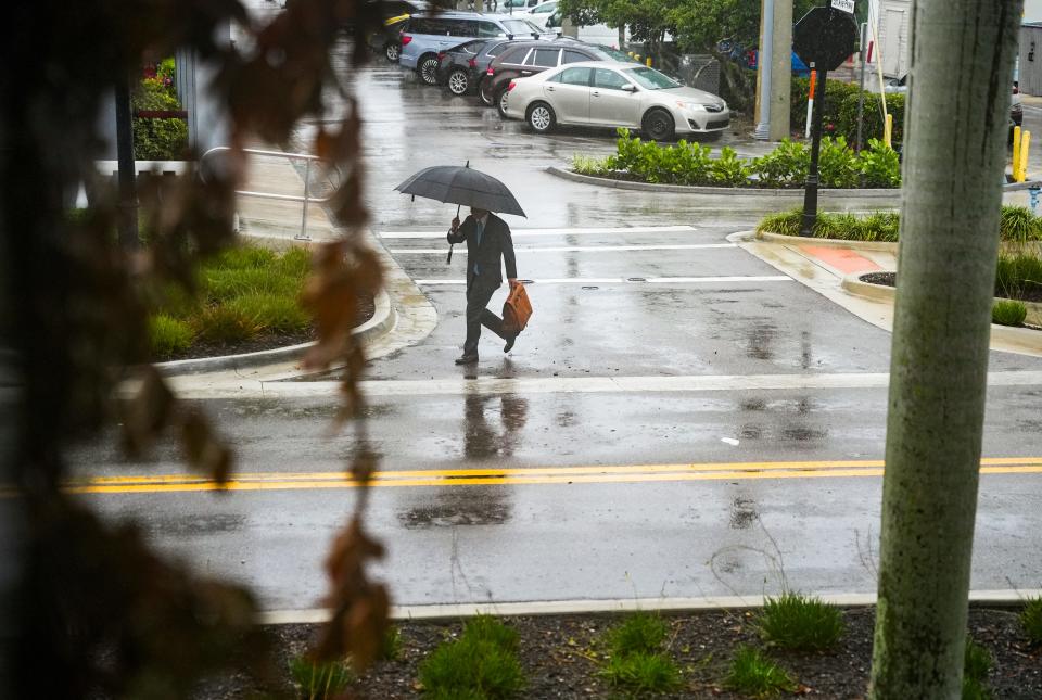 A person walks along Eighth Street South as rain falls in Naples on Tuesday, June 11, 2024.