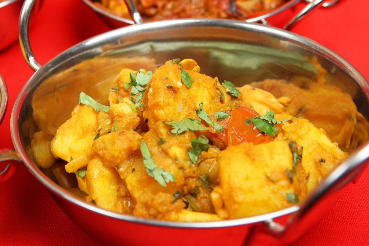 Potato curry in a stainless steel handi with a red background