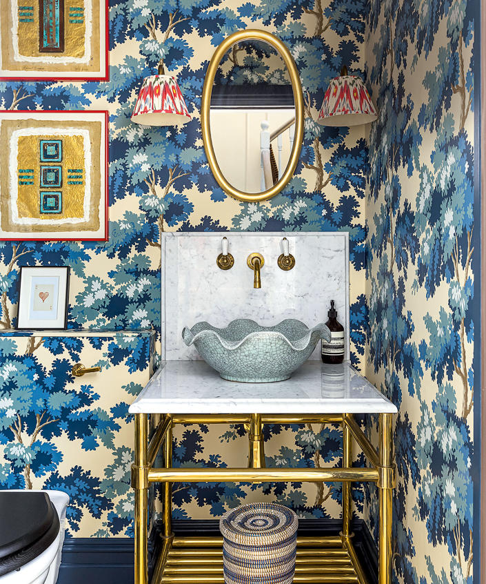 Bold blue floral wallpaper in bathroom with red  wall lights and scalloped shape basin