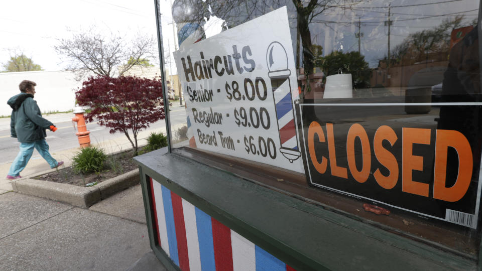 FILE - In this May 6, 2020 file photo, a woman walks past a closed barber shop in Cleveland. Small businesses are in limbo again as the coronavirus outbreak rages and the government’s $659 billion relief program draws to a close. Companies still struggling with sharply reduced revenue are wondering if Congress will give them a second chance at the Paycheck Protection Program, which ends Friday, Aug. 7, after giving out 5.1 million loans worth $523 billion. (AP Photo/Tony Dejak, File)