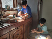 In this Sunday, April 19, 2020 photo provided by Anil Sanweria, his sons, Uddhav Pratap, 8, left, and Advait Vallabh, 9, help in the kitchen during a nationwide COVID-19 coronavirus lockdown. The brothers believe the lockdown should continue for a year. “They shouldn’t reopen till the time there are zero cases left,” the younger Uddhav Pratap says. (Anil Sanweria via AP)