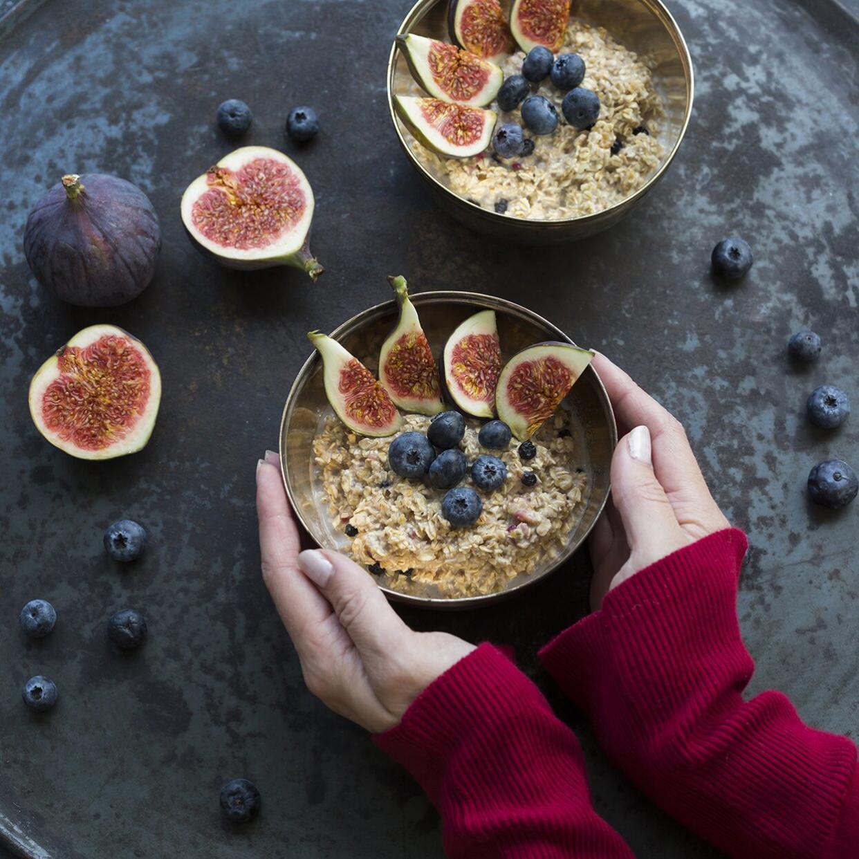 Woman's hands holding bowl of porridge with sliced figs, blueberries and dried berries