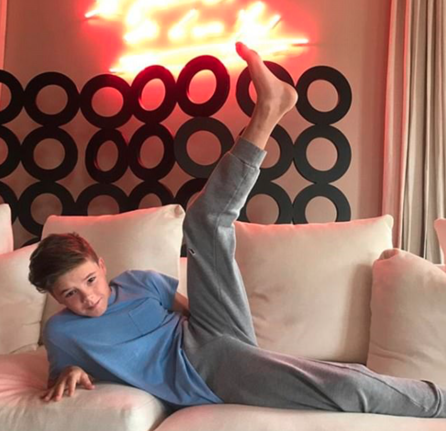 Cruz copies his mums signature pose sitting on a lush cream sofa in front of a neon Tracey Emin artwork. Source: Instagram