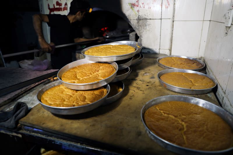 A baker takes dishes of rawani dessert out of a wood-fired oven during the holy month of Ramadan in Sanaa