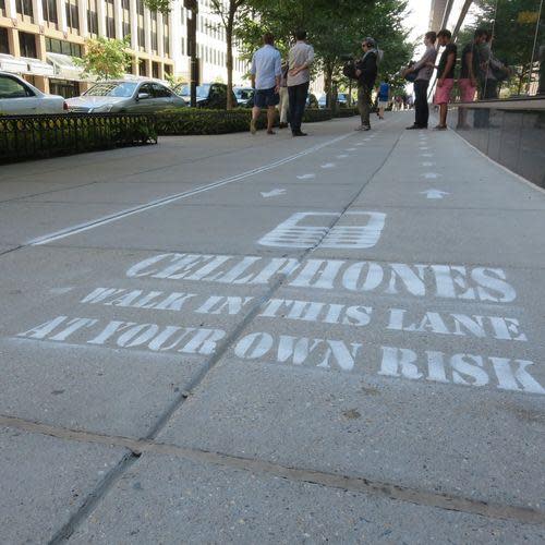 Street stenciled with 'CELLPHONES WALK IN THIS LANE AT YOUR OWN RISK