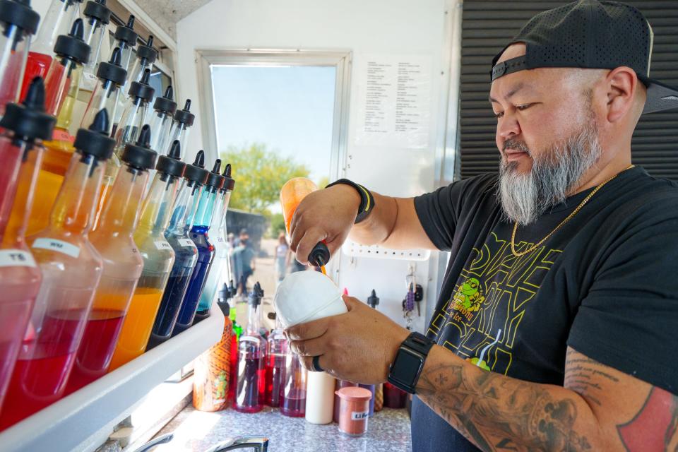 Owner, Desmond Martin adds flavors to shaved ice in the Happy Honu Shave Ice truck on April 16, 2022, at the Arrowhead Farmers Market in Glendale, Ariz.