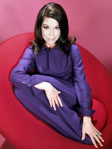 Dressed in a purple jumpsuit, Moore lounges on a red chair for a 1970 photoshoot.