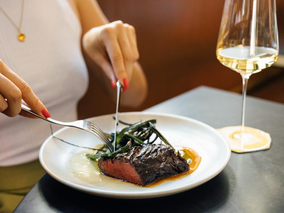 A person eating a plate of charcoal grilled steak, spring onions, and romesco verde.