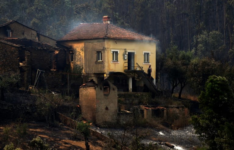 A man stands in the stairway of a house with smoke billowing from the roof in an area devastated by a wildfire in Canical, near Alvares, on May 18, 2017