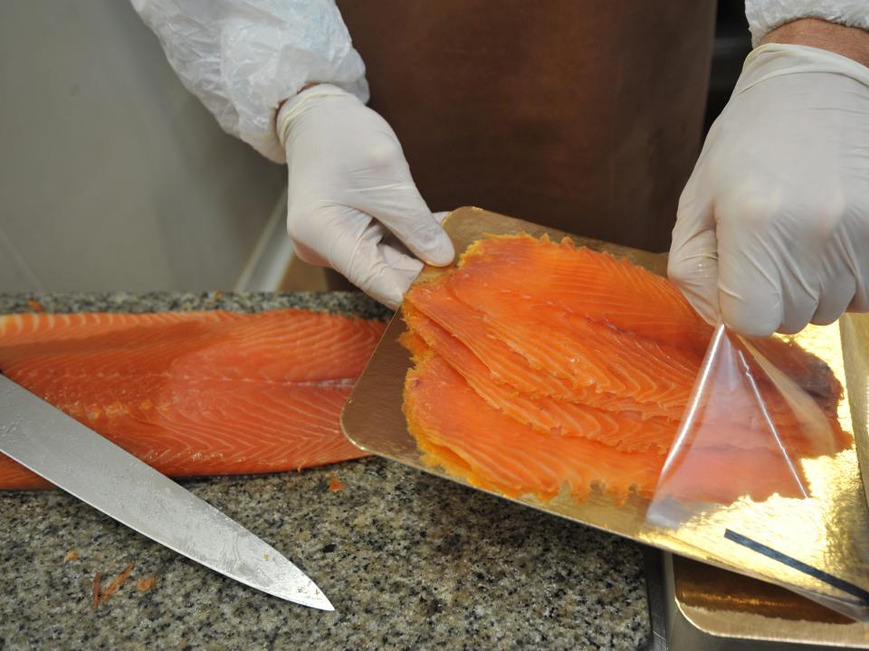 a person wearing gloves handling slices of smoked salmon