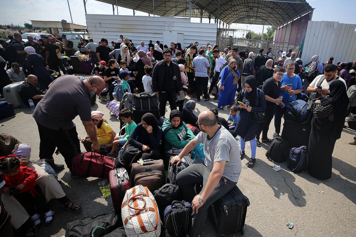 A crowd of people, some of them sitting on suitcases, is gathered by the border crossing into Egypt.