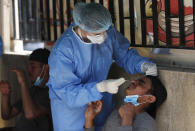 In this Saturday, May 23, 2020 photo, a nurse tests a Bangladeshi worker for the coronavirus, near a building where dozens of foreign workers living in overcrowded apartments have tested positive for the coronavirus, in Beirut, Lebanon. Some 250,000 registered migrant laborers in Lebanon — maids, garbage collectors, farm hands and construction workers — are growing more desperate as a crippling economic and financial crisis sets in, coupled with coronavirus restrictions. With no functioning airports and exorbitant costs of repatriation flights, many are trapped, unable to go home. (AP Photo/Hussein Malla)