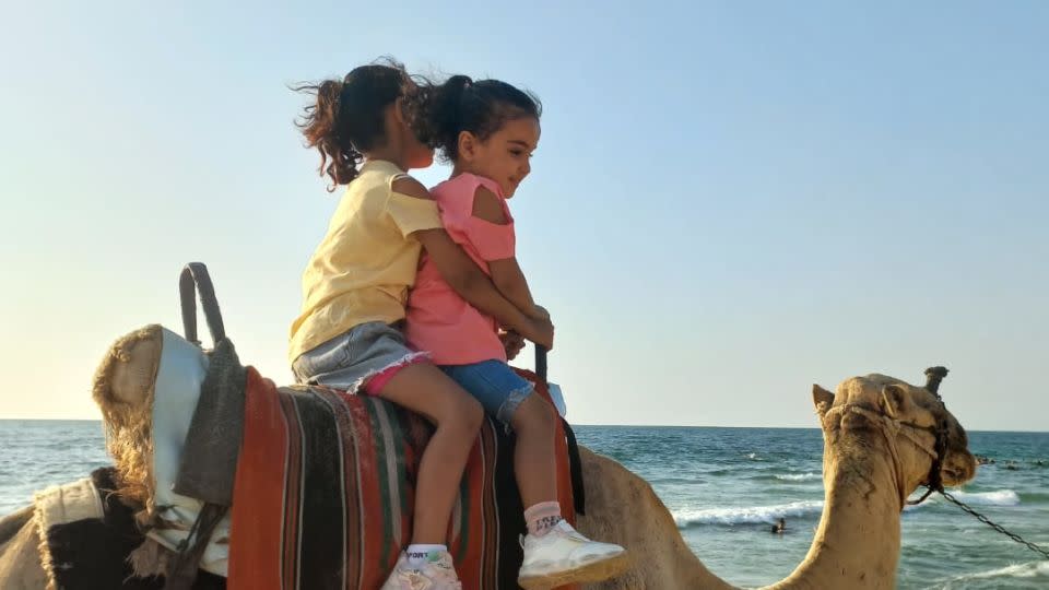 Palestinian siblings Ella Mohammed Hamouda (left) and Sila Mohammed Hamouda (right) ride a camel on a beach in northern Gaza, on October 6, 2023. - Mohammed Hamouda