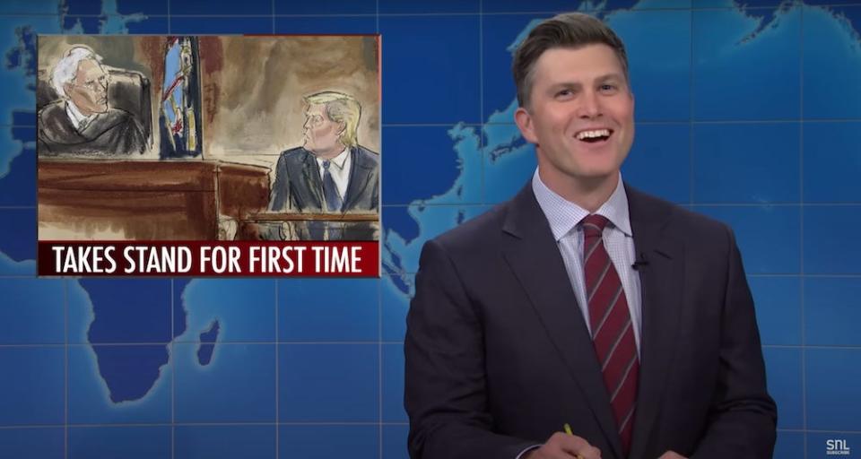 A screenshot from SNL "Weekend Update" from October 31, 2023, showing Colin Jost smiling with one of Elizabeth William's courtroom sketches of Donald Trump inset.