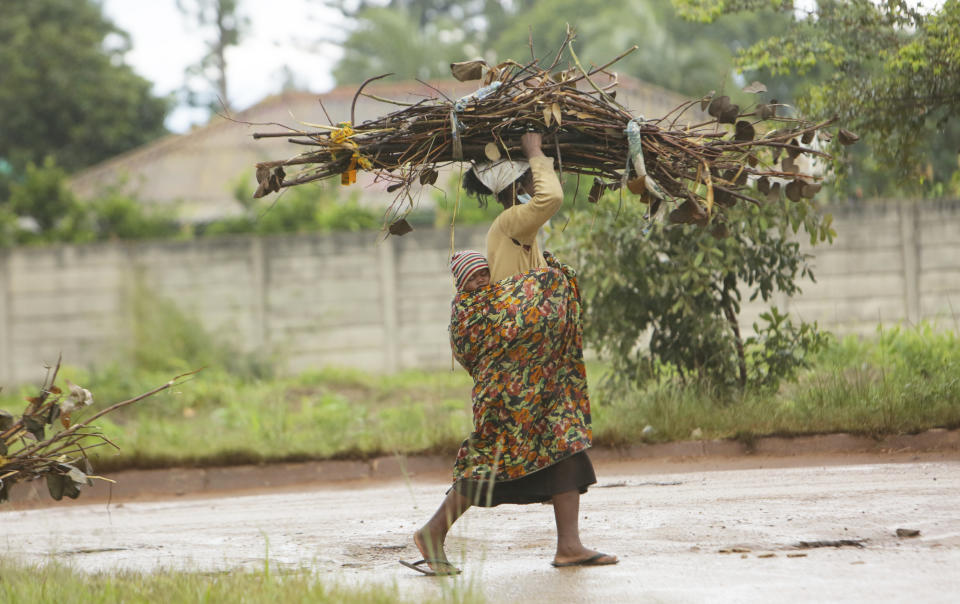 A woman with a baby strapped on her back carries firewood for cooking on the streets of Harare, in this Tuesday, March 2, 2021 photo. From driving trucks and fixing cars to encouraging girls living with disability to find their places in society, women in Zimbabwe are refusing to be defined by their gender or circumstances, even as the pandemic hits them hardest and imposes extra burdens.(AP Photo/Tsvangirayi Mukwazhi)