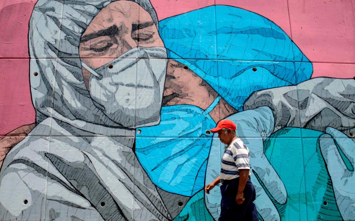 A man walks past a coronavirus-related mural, in Acapulco, Guerrero State, Mexico -  FRANCISCO ROBLES/AFP