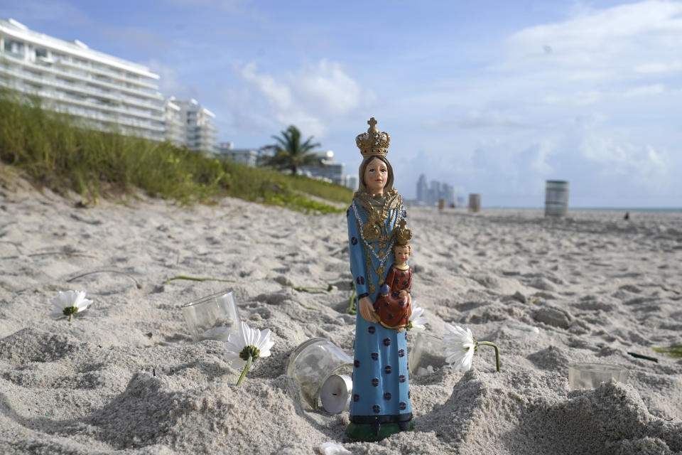 A statue sits on the beach with candles and flower petals near the Champlain Towers South Condo building, Saturday, June 26, 2021, in the Surfside area of Miami. The apartment building partially collapsed on Thursday. (AP Photo/Lynne Sladky)