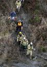 Volunteers and firefighters with chainsaws and hand tools hike down a rugged path toward the scene of a deadly mudslide, Tuesday, March 25, 2014, in Oso, Wash. At least 14 people were killed in the 1-square-mile slide that hit in a rural area about 55 miles northeast of Seattle on Saturday. Several people also were critically injured, and homes were destroyed. (AP Photo/Elaine Thompson)