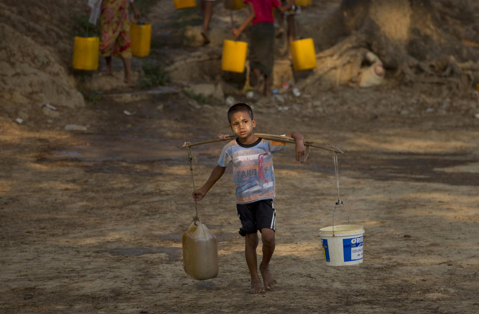 In this April 4, 2014 photo, 8-year old Ko Thu Ra carries drinking water in plastic containers from a natural water pond in Dala, suburbs of Yangon, Myanmar. “I’m only eight years old and it’s so tiring for me to carry water” said Thu Ra. During Myanmar’s annual dry season in April and May residents walk up to five kilometers (three miles) carrying buckets full of water from a natural pond, the only source for drinking water in this improvised neighborhood. (AP Photo/Gemunu Amarasinghe)