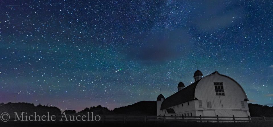 A meteor shower is pictured against a starry sky and picturesque foreground