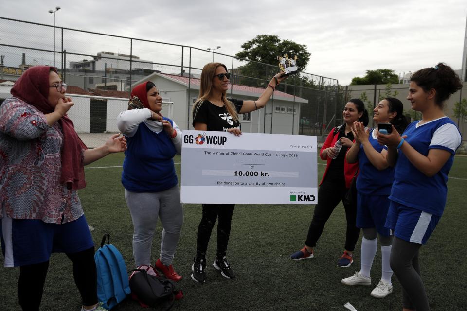 In this Wednesday, May 22, 2019 photo, Katerina Salta, Sport for Protection Program Manager holds the Global Goals World Cup trophy as members Hestia FC Women's Refugee Soccer team applaud in Athens. Many of the players at Hestia FC weren't allowed to play or even watch soccer matches in their home countries. Hestia FC was set up by the Olympic Truce Centre, a non-government organization created in 2000 by the International Olympic Committee and Greek Foreign Ministry. (AP Photo/Thanassis Stavrakis)