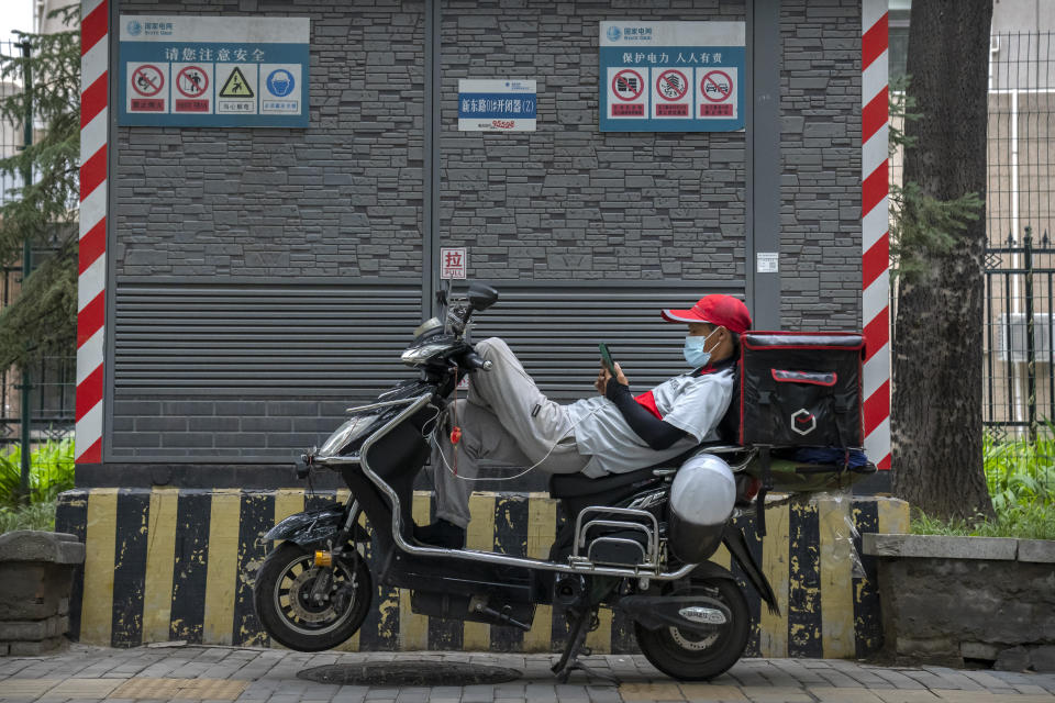 A delivery driver wearing a face mask to prevent the spread of COVID-19 rests on his scooter between calls in Beijing, Saturday, July 17, 2021. (AP Photo/Mark Schiefelbein)