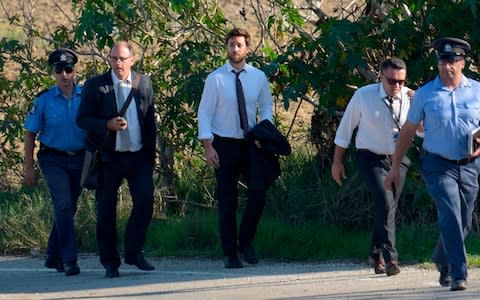 Matthew Caruana Galizia (C) and Peter Caruana Galizia (2ndL), son and husband of journalist Daphne Caruana Galizia, walk with policemen past the wreckage of her, which was blown up by a bomb on Monday.  - Credit: AFP