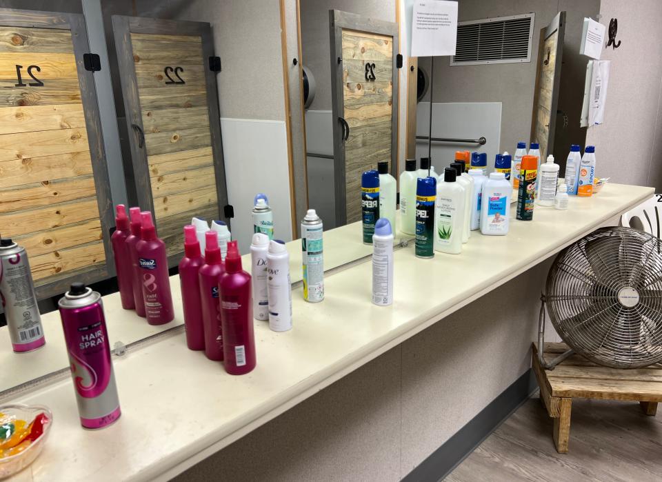 Hair products lined up on a counter with a mirror view of bathroom stalls in the background