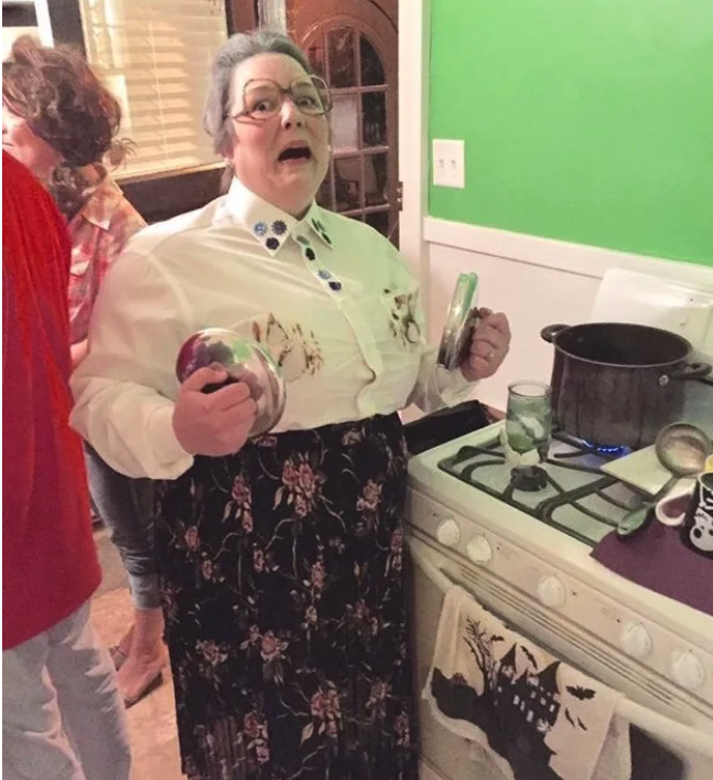 Someone dressed as an old Mrs Doubtfire while holding pot handles next to her scorched chest