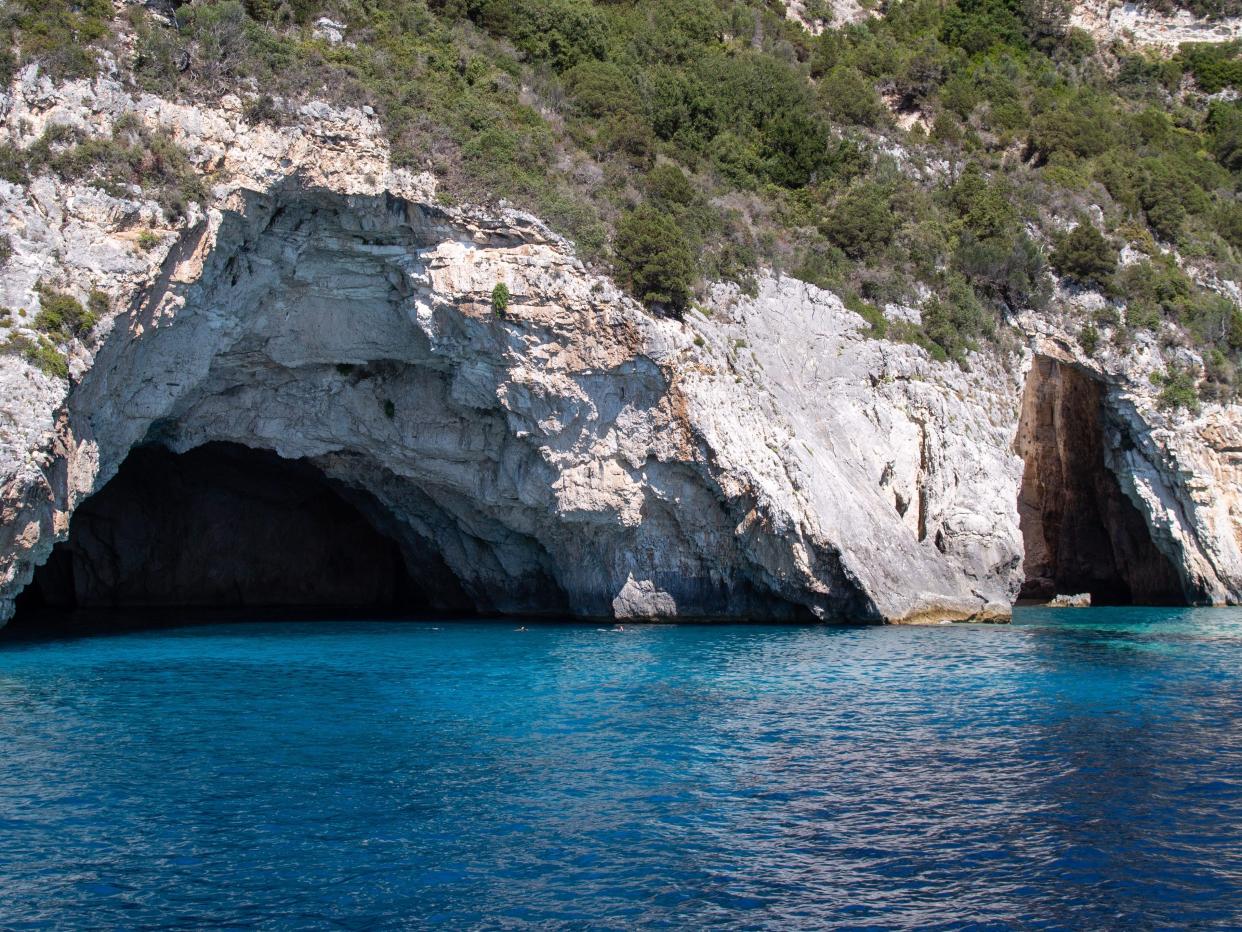 caves over bright blue waters in paxos greece